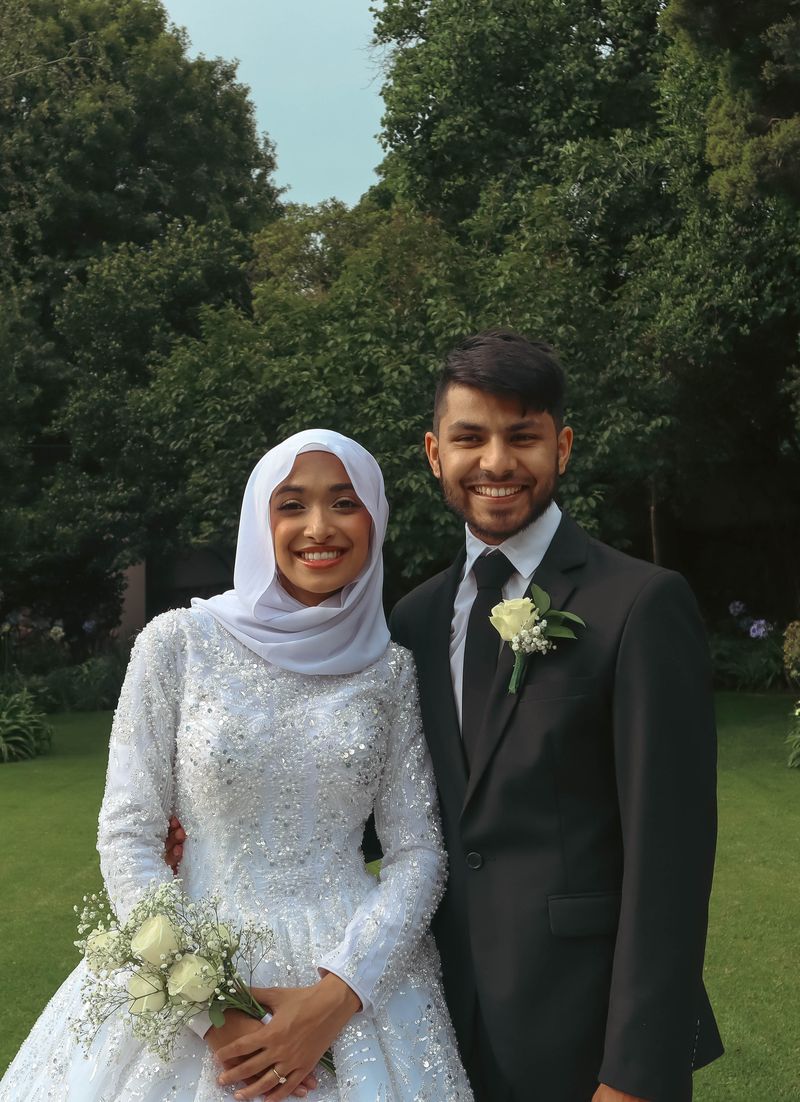 A bride and groom smiling together in a garden, the bride holding a bouquet