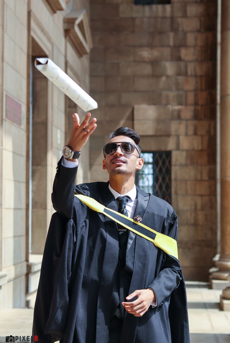 A graduate throwing his diploma scroll into the air outside a sandstone university building